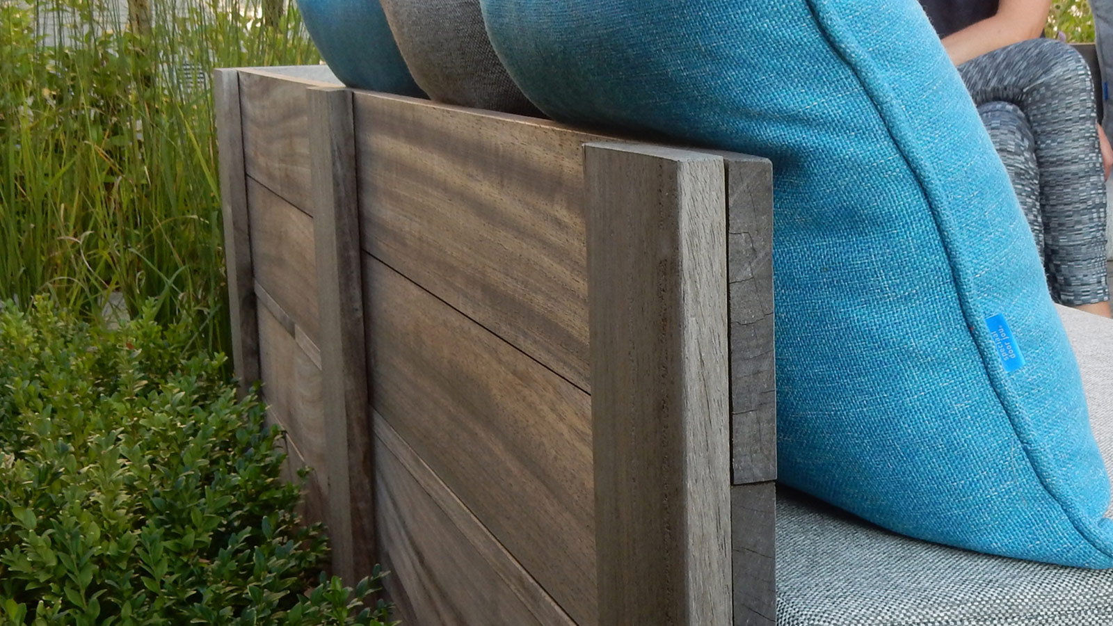 Houten terras in padouk met zitbanken op maat met kussens in een vrolijke accentkleur.